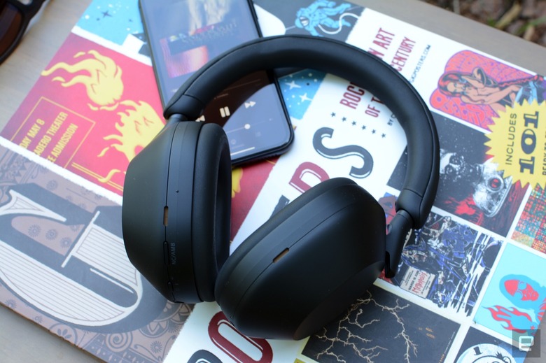 A pair of black headphones, the Sony WH-1000XM5, rest on top of a book and a smartphone.