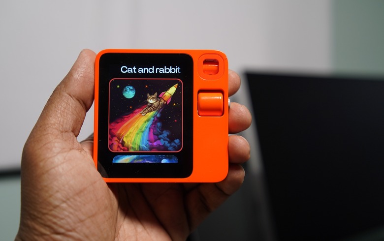 A hand holding a small square orange device with a display.
