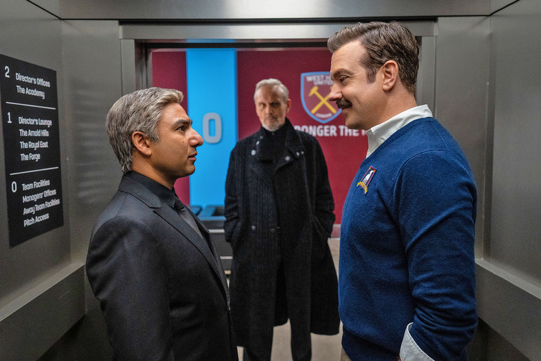 In this teaser image from 'Ted Lasso' season 3, Ted faces down another character in a cramped hallway while a figure in a long black coat looks on.