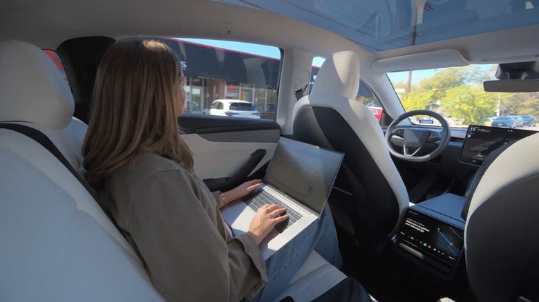 A woman using a laptop in the passenger seat of a Tesla robotaxi