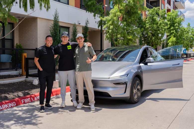 Tesla reps and customer stand in front of a Model Y that was delivered using the robotaxi service.