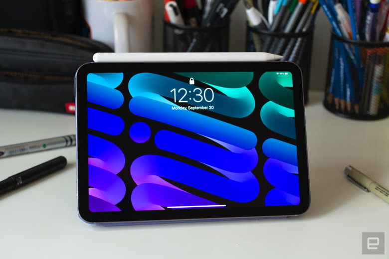 Photo of the 6th-generation iPad mini sitting on a desk with its Apple Pencil magnetically attached to its side. Its colorful blue / green lock screen (with cursive 