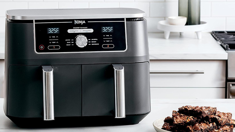 The ninja foodi 10-quart air fryer sits on a countertop with a plate of brownies nearby.