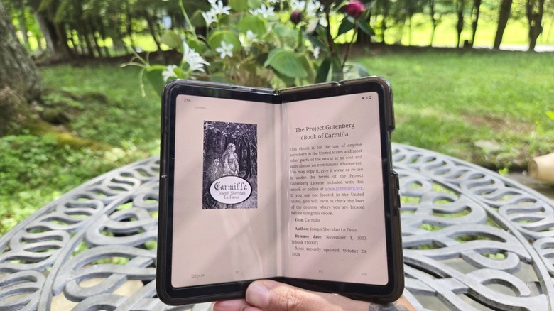 A foldable phone is pictured open but slightly bent, book-style, with an ebook version of the novella Carmilla displayed on it