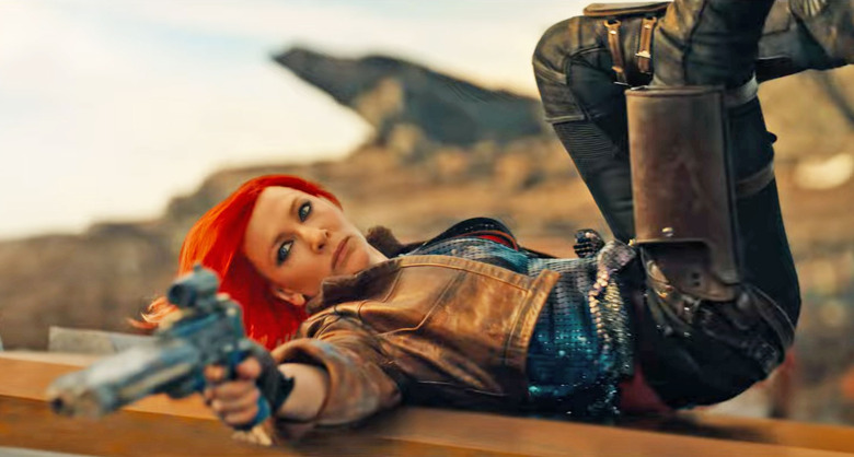 Cate Blanchett as Lilith in the movie Borderlands. In this action still, she lays on her back with legs in the air and aims a gun towards someone off camera.