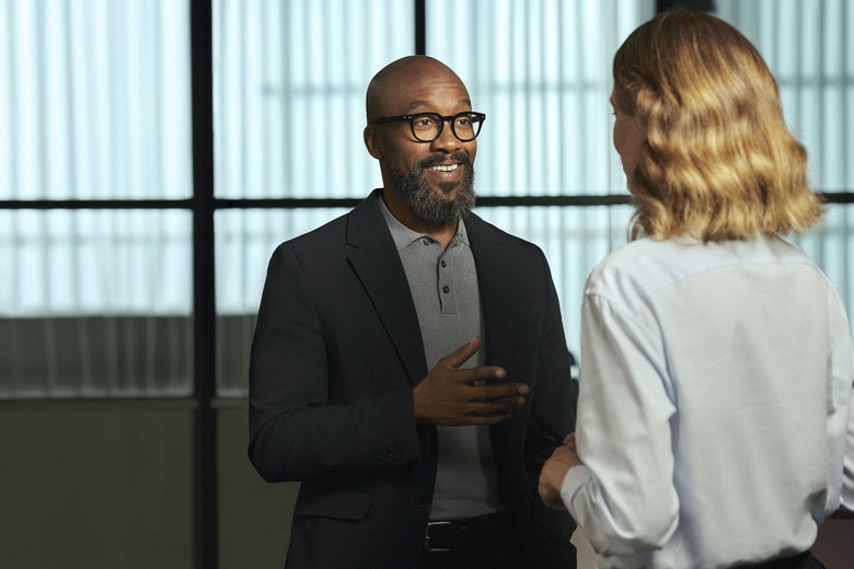 A man wearing Nuance Audio glasses and speaking to a woman facing away from the camera.
