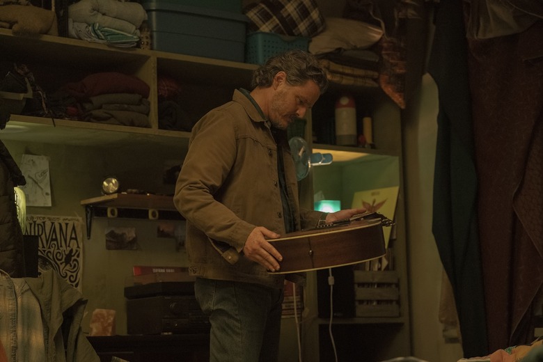 A man looks down at an acoustic guitar he's holding.