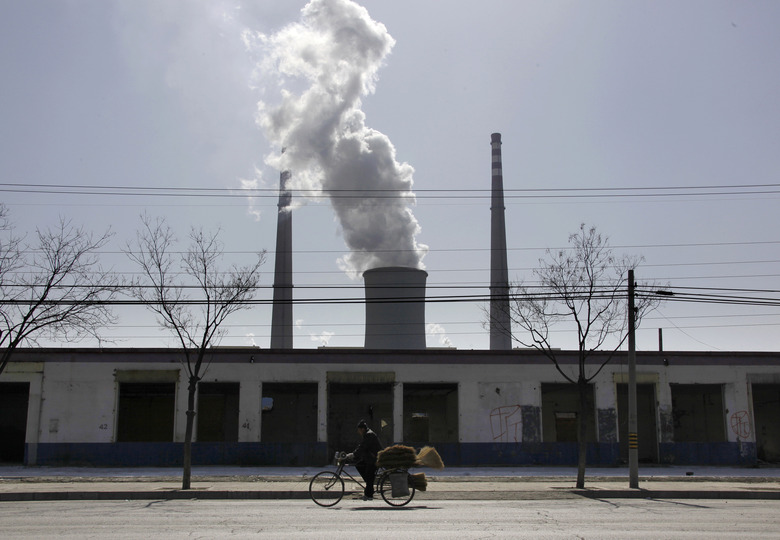 A man selling brooms rides his bicycle past abandoned buildings in front of a chimney billowing smoke from a nearby coal-burning power station in Beijing March 10, 2010. China signed up, along with India, to the Copenhagen Accord for fighting climate change on Tuesday, joining almost all other major greenhouse gas emitters in endorsing the non-binding pact. REUTERS/David Gray (CHINA - Tags: POLITICS ENVIRONMENT BUSINESS)