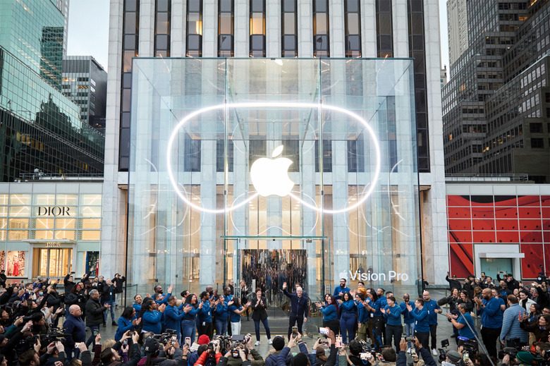 The facade of an Apple Store with the Apple logo lit up and surrounded by the shape of the Vision Pro headset.