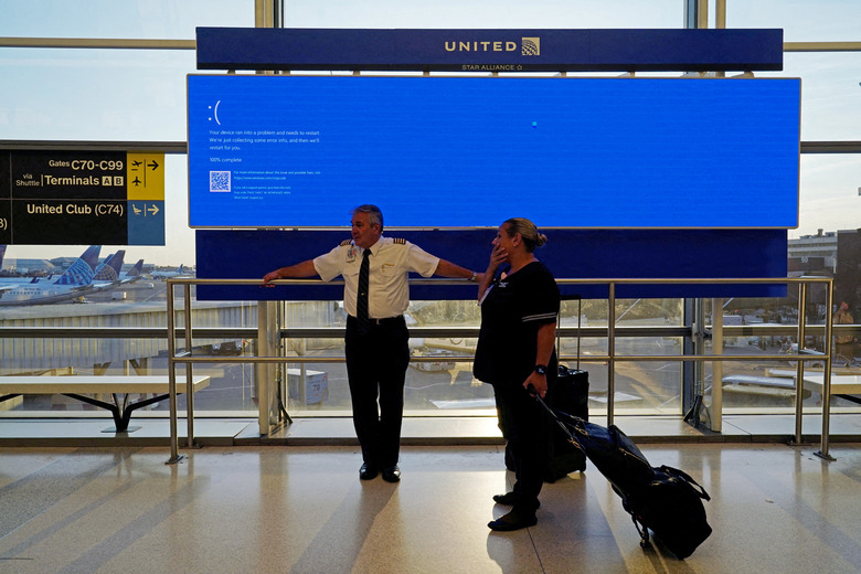 United Airlines employees wait by a departures monitor displaying a blue error screen, also known as the “Blue Screen of Death” inside Terminal C in Newark International Airport, after United Airlines and other airlines grounded flights due to a worldwide tech outage caused by an update to CrowdStrike's 