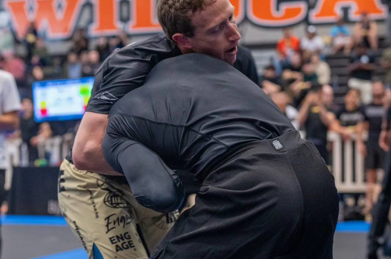Two people in a fight, one has the other in a headlock. There's an audience behind them.