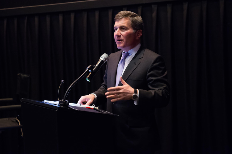 A man in a suit standing behind a podium with a mic.