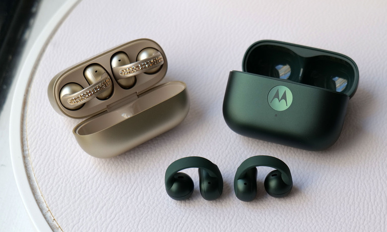 The French Oak and Trekking green Moto Buds Loop earbuds, with the Trekking Green version of the earbuds sitting outside of its charging case.