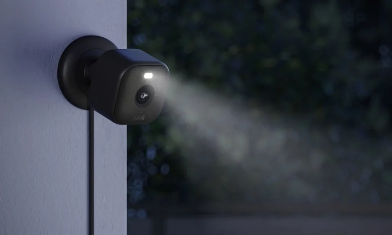 The new Blink Mini 2 camera in black shown mounted to an outside wall at nighttime with the LED spotlight shining