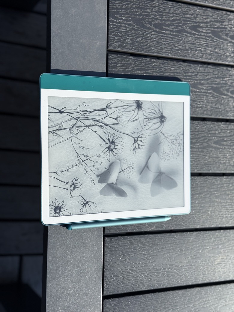 The teal Amazon Kindle Scribe 2 on a wooden table, with a Premium Pen attached to its right edge.