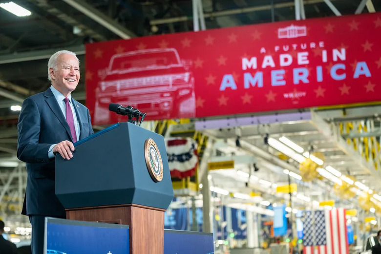 President Joe Biden standing at a podium in an auto factory. A sign behind says 