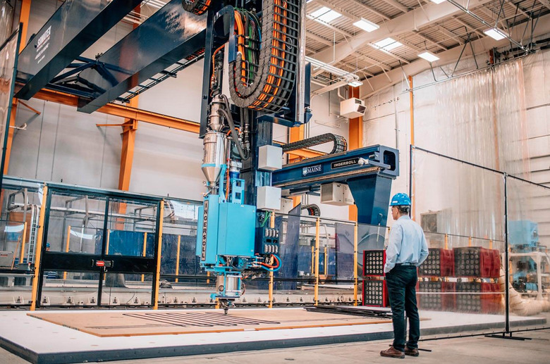 A man stands next to a giant 3D printer.