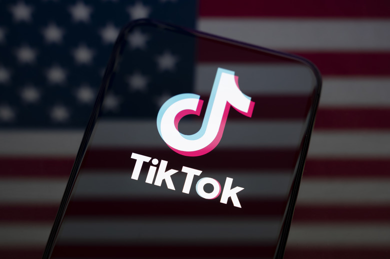 The TikTok logo displays on the screen of a smartphone placed on a reflective surface onto which the US flag is projected. The social network TikTok experiences technical failures and massive malfunctions following the acquisition and transfer of the Chinese app by an American consortium, in Creteil, France, on January 27, 2026. (Photo by Samuel Boivin/NurPhoto via Getty Images)