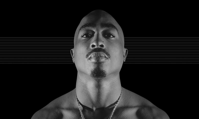 Photo of the late Tupac Shakur, staring down at the camera against a black background with subtle horizontal gray lines.