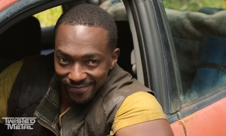 Anthony Mackie as John Doe in the trailer for Peacock’s ‘Twisted Metal’ series. He sits in the driver’s seat of a car, looking outward with a wry grin.