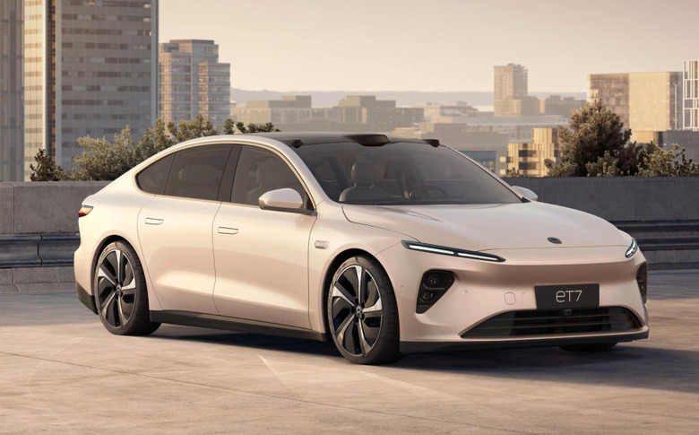 Marketing image of the Nio ET7 EV. The goldish-beige car sits on a lot overlooking a city skyline during daytime.