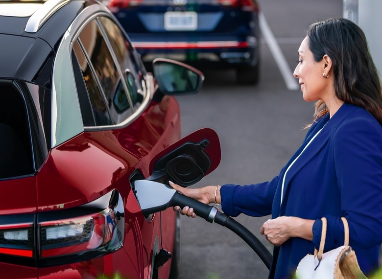 A person smiles as they place a charging cable into an electric vehicle. 