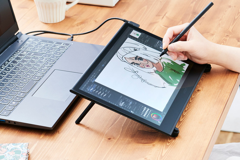 An artist draws on a Wacom Movink pen display that's connected to a black laptop.