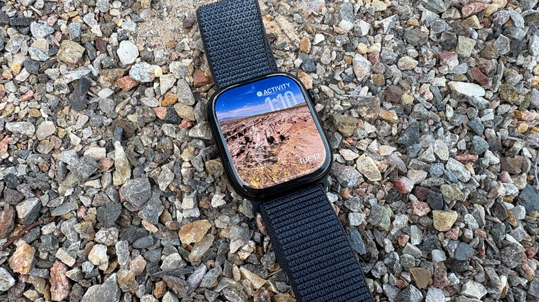 An Apple Watch Series 10 running the public beta of watchOS 26. The watch sits on gravel and shows a picture of mountains and sky