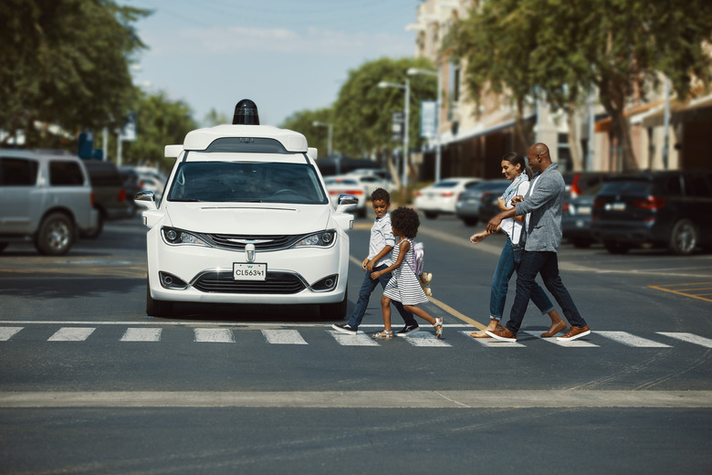 A Waymo autonomous vehicle waits for a family of pedestrians to cross the street.