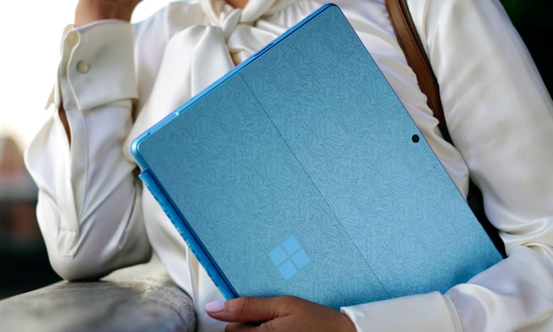 Lifestyle image of the Microsoft Surface Pro 9. A person holds a blue (patterned) version of the hybrid device (back-facing).