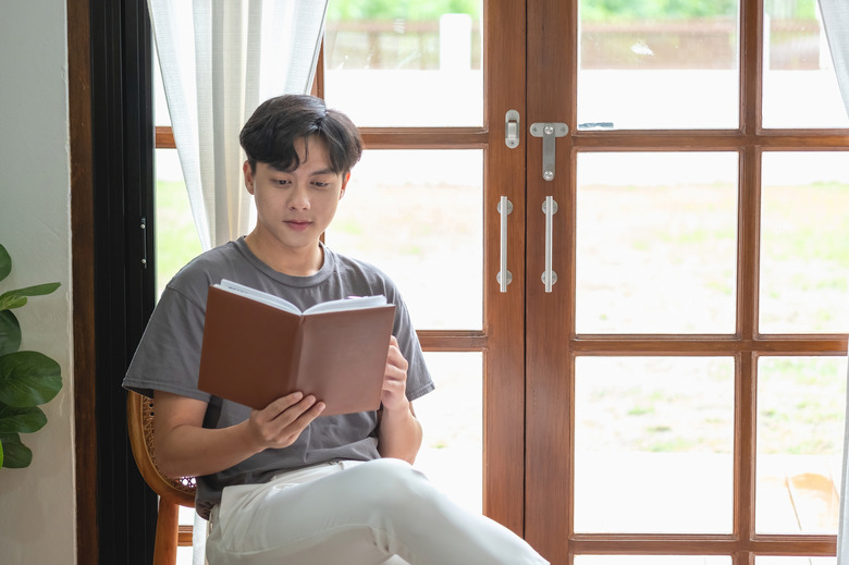 Portrait of a white man sitting inside the house reading and drinking coffee to relax on vacation.