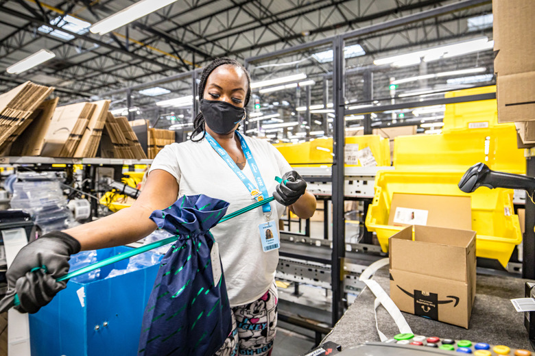 A woman packs an Amazon order. Amazon boxes with the company's arrow logo are scattered in the background.