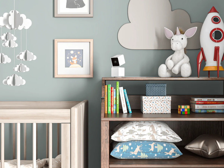 A security camera on top of a shelf in a room with baby blue walls and a crib.