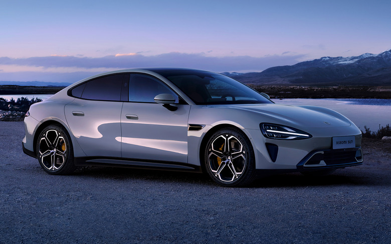 The Xiaomi SU7 electric sedan in gray is parked at dusk on a gravel road.