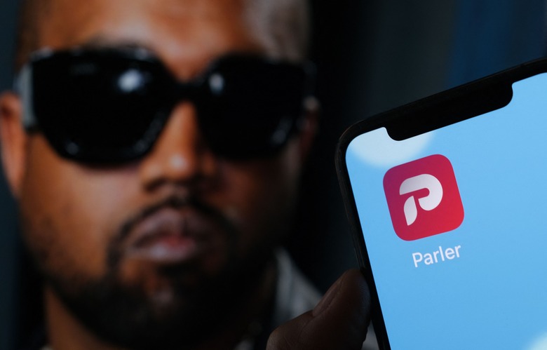 This illustration photo shows the Parler social network app logo on a cell phone screen with a picture of US rapper Kanye West in the background in Los Angeles, October 17, 2022. - Social network Parler announced on October 17 a deal for Kanye West to buy the platform popular with US conservatives, just over a week after the rapper's Twitter and Instagram accounts were restricted over anti-Semitic posts. West -- now known as Ye -- has recently alienated fans and business partners with anti-Semitic comments, interest in racist conspiracy theories and wearing a provocative 