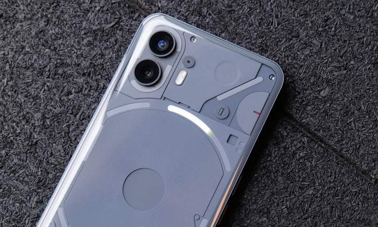 Photo of the Nothing Phone 2 smartphone. Closeup, showing its top and center sections framed at an angle. It sits on a dark surface.
