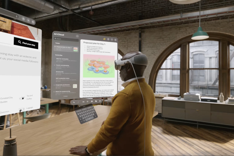 A man wears a Vision Pro headset and looks at various apps overlaid over a room