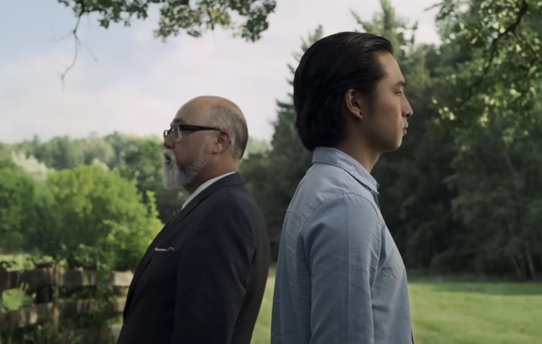 One man wearing a blue button down and a man wearing a black suit, their backs turned on each other.