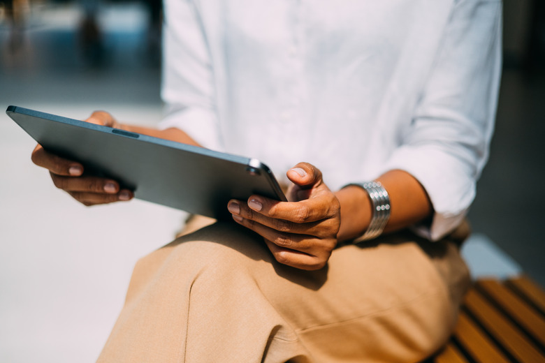 A close up view of an unrecognizable Latin entrepreneur read something on her tablet while sitting on the street bench.
